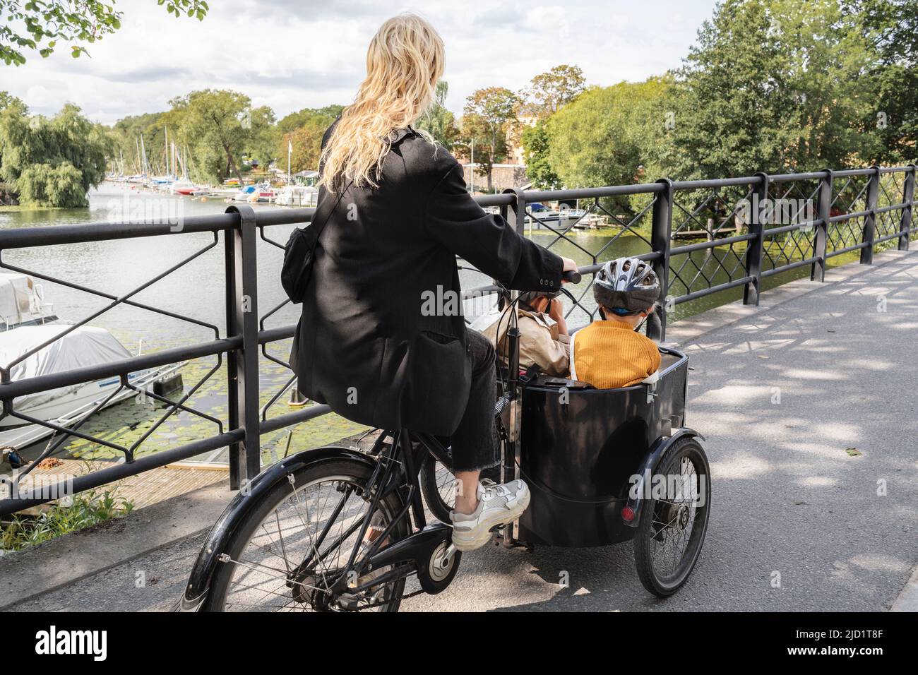 Mother riding bicycle with children in carriage Stock Photo