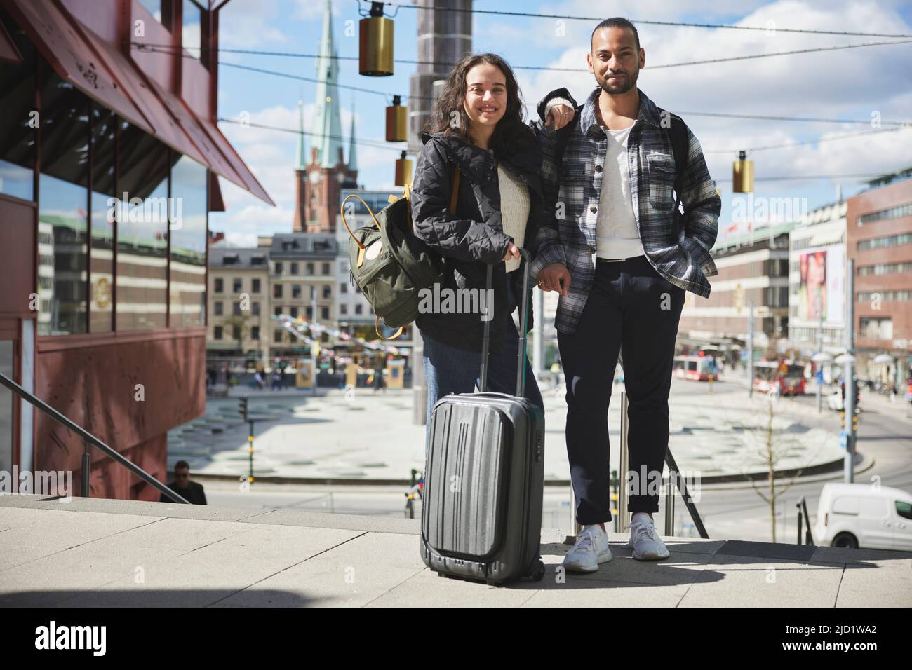 Portrait of smiling man and woman with luggage in city center Stock Photo