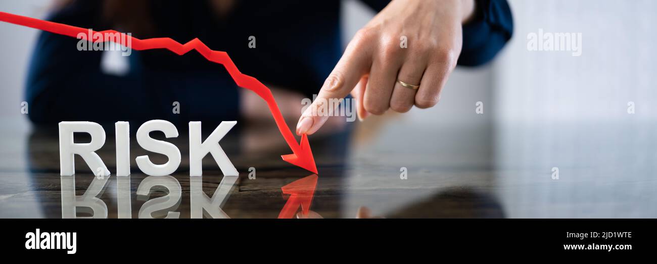 Businesswoman Pointing Red Diminishing Arrow Over The Risk Text On Reflective Desk Stock Photo