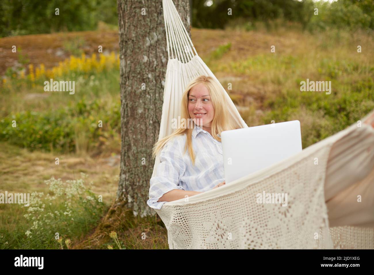 Woman using laptop on hammock Stock Photo