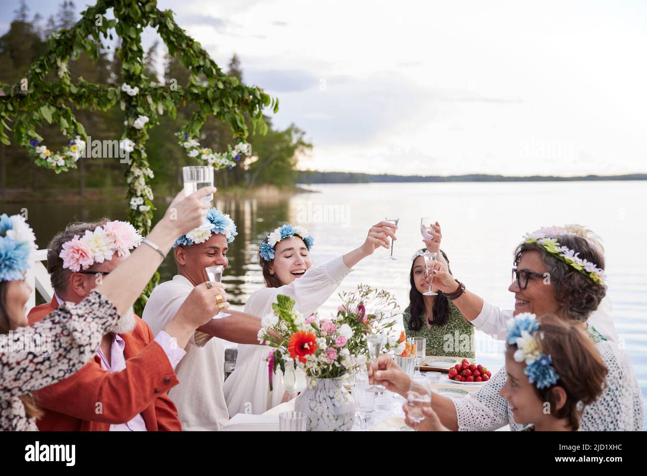 Family raising toast during midsummer dinner by lake Stock Photo