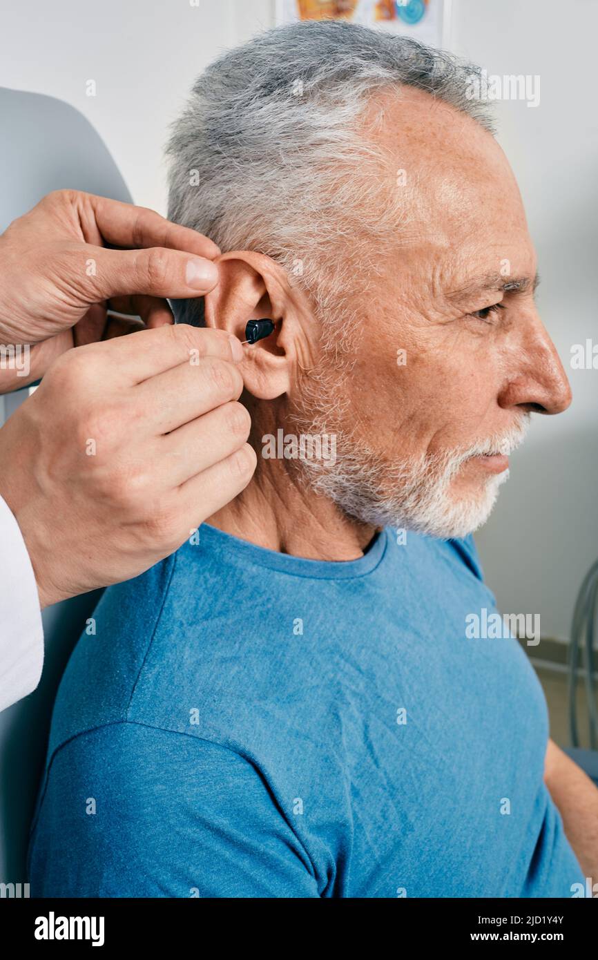 Senior man while installation hearing aid into his ear by his audiologist, close-up. Hearing treatment for hearing impaired people Stock Photo