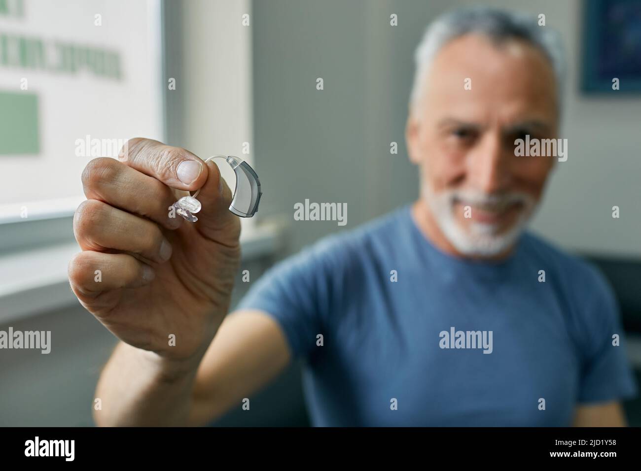 Senior man holding BTE hearing aid in hand on foreground, close-up. Treatment of deafness in elderly people Stock Photo