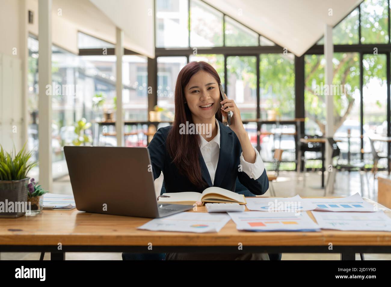 Smiling business asian woman in black suit talking on phone Stock Photo