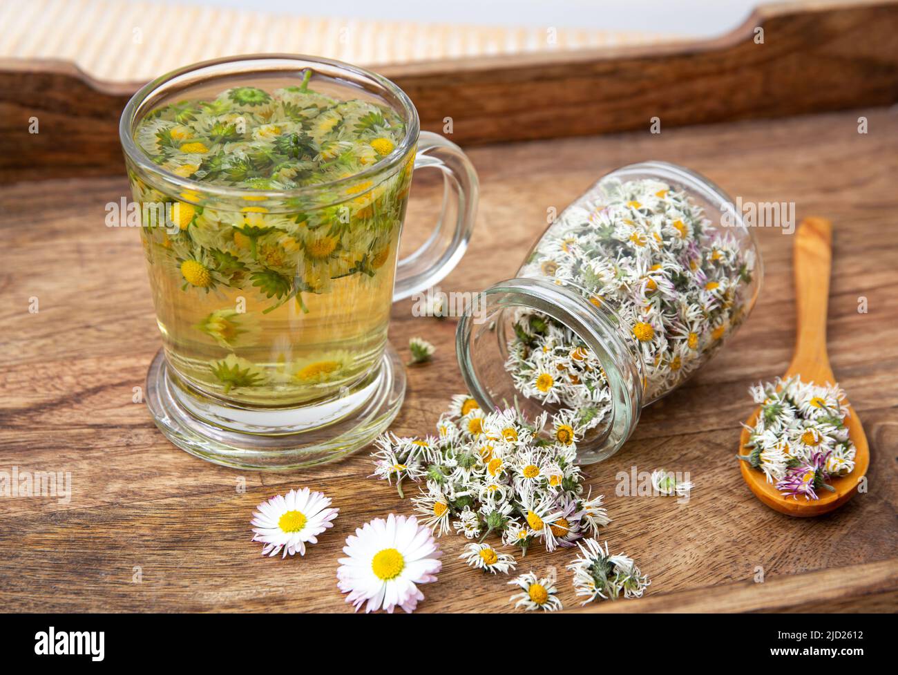 Dried herbal medicinal plant Common Daisy, also known as Bellis Perennis. Dry flower blossoms in glass jar and and herbal tea in glass, indoors still Stock Photo