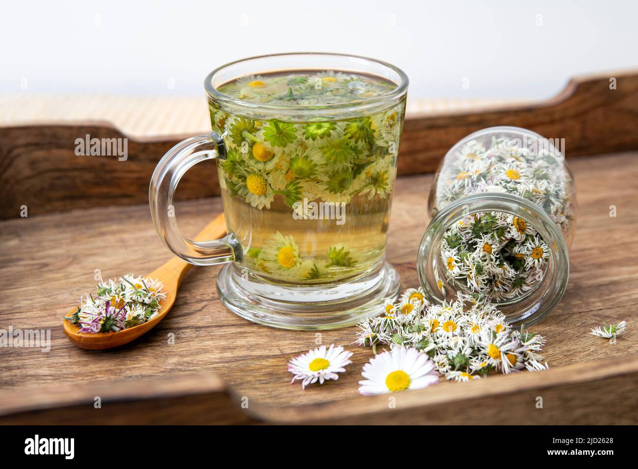 Dried herbal medicinal plant Common Daisy, also known as Bellis Perennis. Dry flower blossoms in glass jar and and herbal tea in glass, indoors still Stock Photo