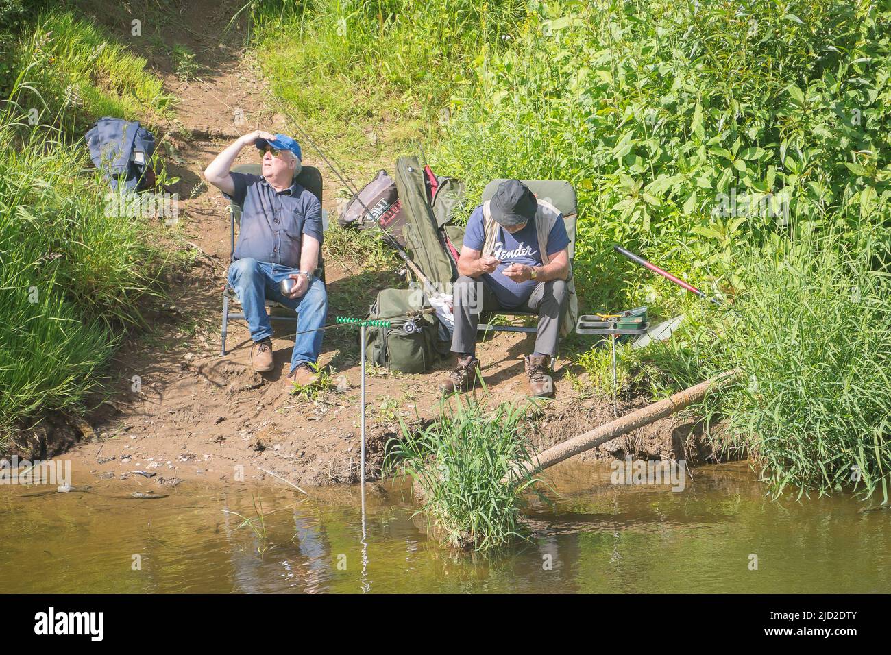 Arley, UK. 17th June, 2022. UK weather: very warm temperatures and bright skies offer the perfect time for a little fishing. Two men sit along a riverside relaxing with fishing rods in the river. Credit: Lee Hudson/Alamy Live News Stock Photo