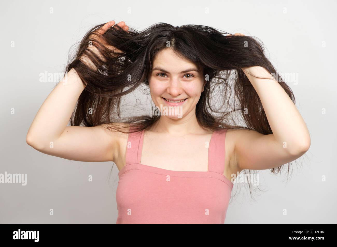 A beautiful brunette woman with long hair on a white background holds her hands on her head and thinks about what hairstyle to do Stock Photo