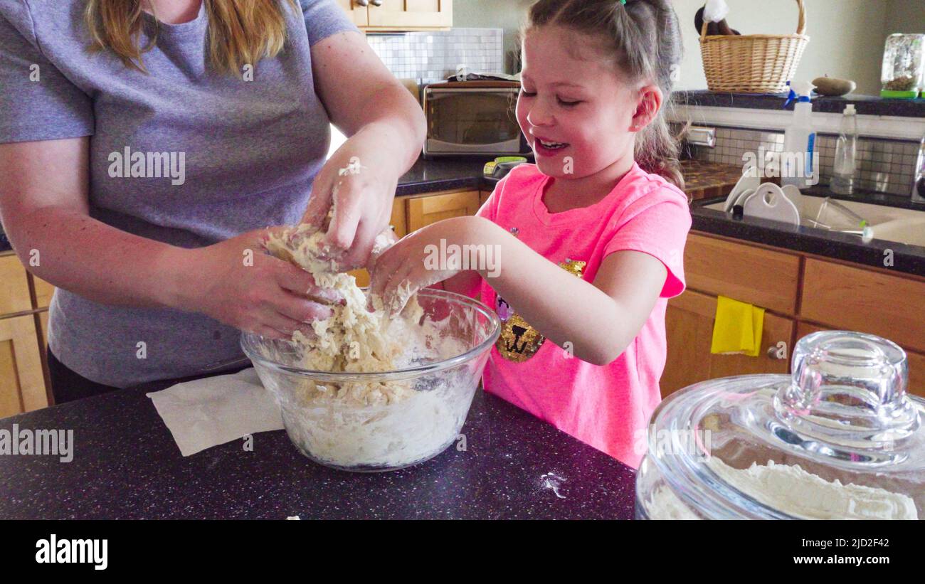 Little girl baking flatbread with her mother in the kitchen Stock Photo