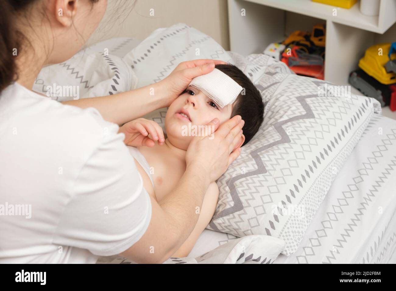 The mother cares for the feverish 4-year-old son, the child has a cooling compress on the forehead Stock Photo