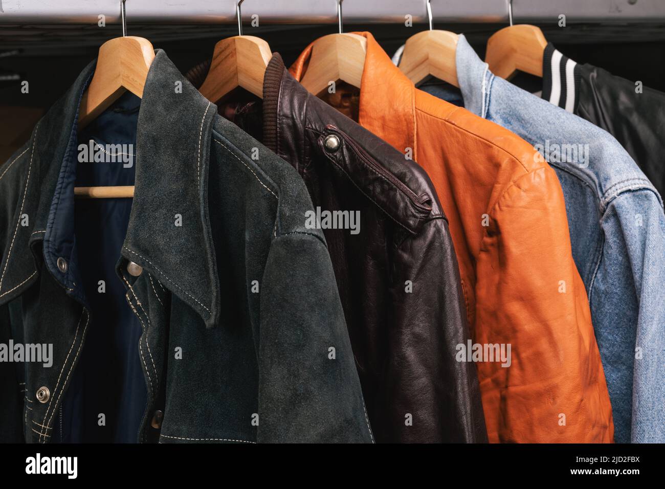 Various vintage suede leather and jeans jackets on hanger rack in a used goods store. Thrifting and sustainability in clothing concept Stock Photo