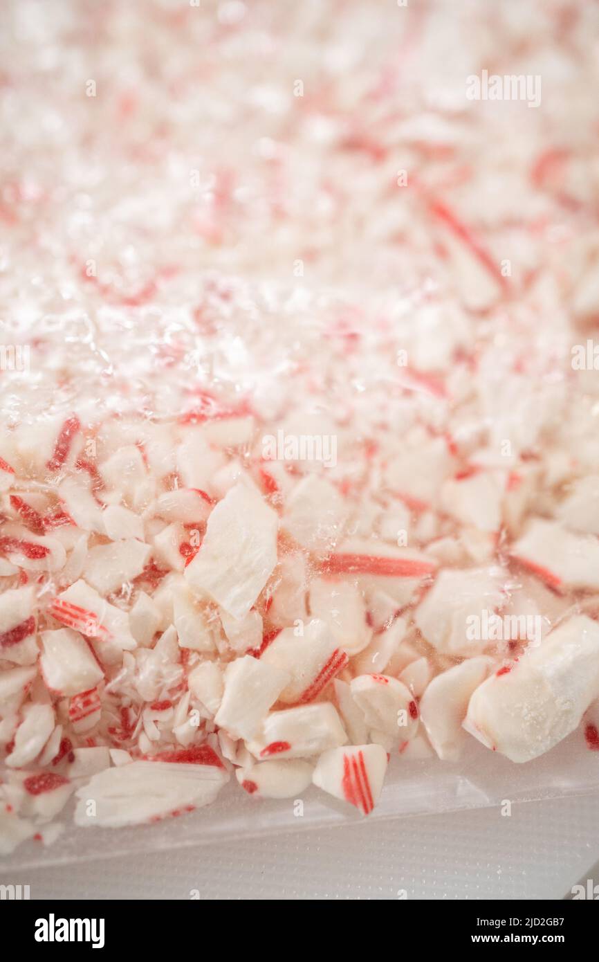 Crushing peppermint candies in a plastic bag with a marble rolling pin on a white cutting board