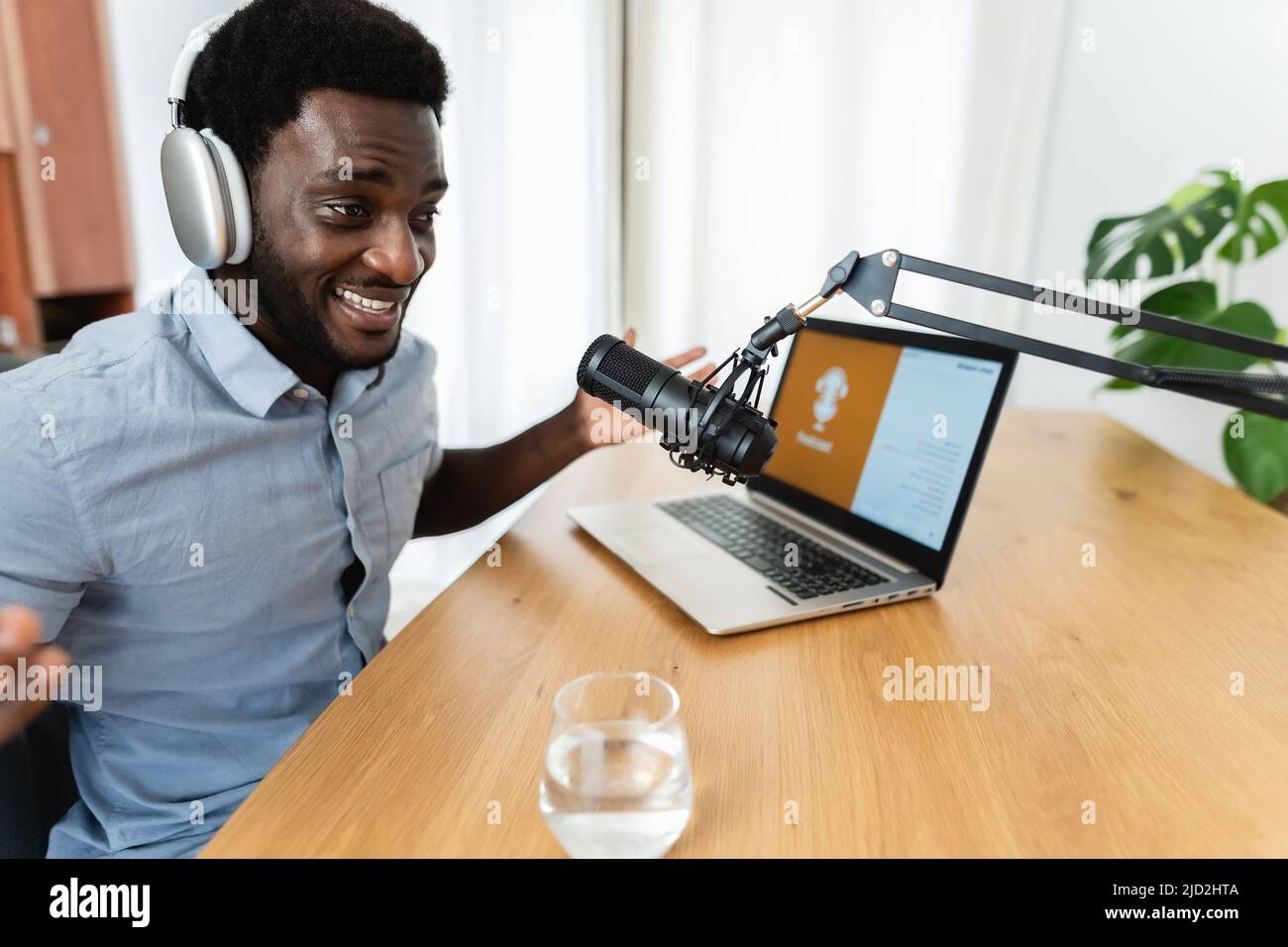 African man recording a podcast using microphone and laptop from his home studio Stock Photo