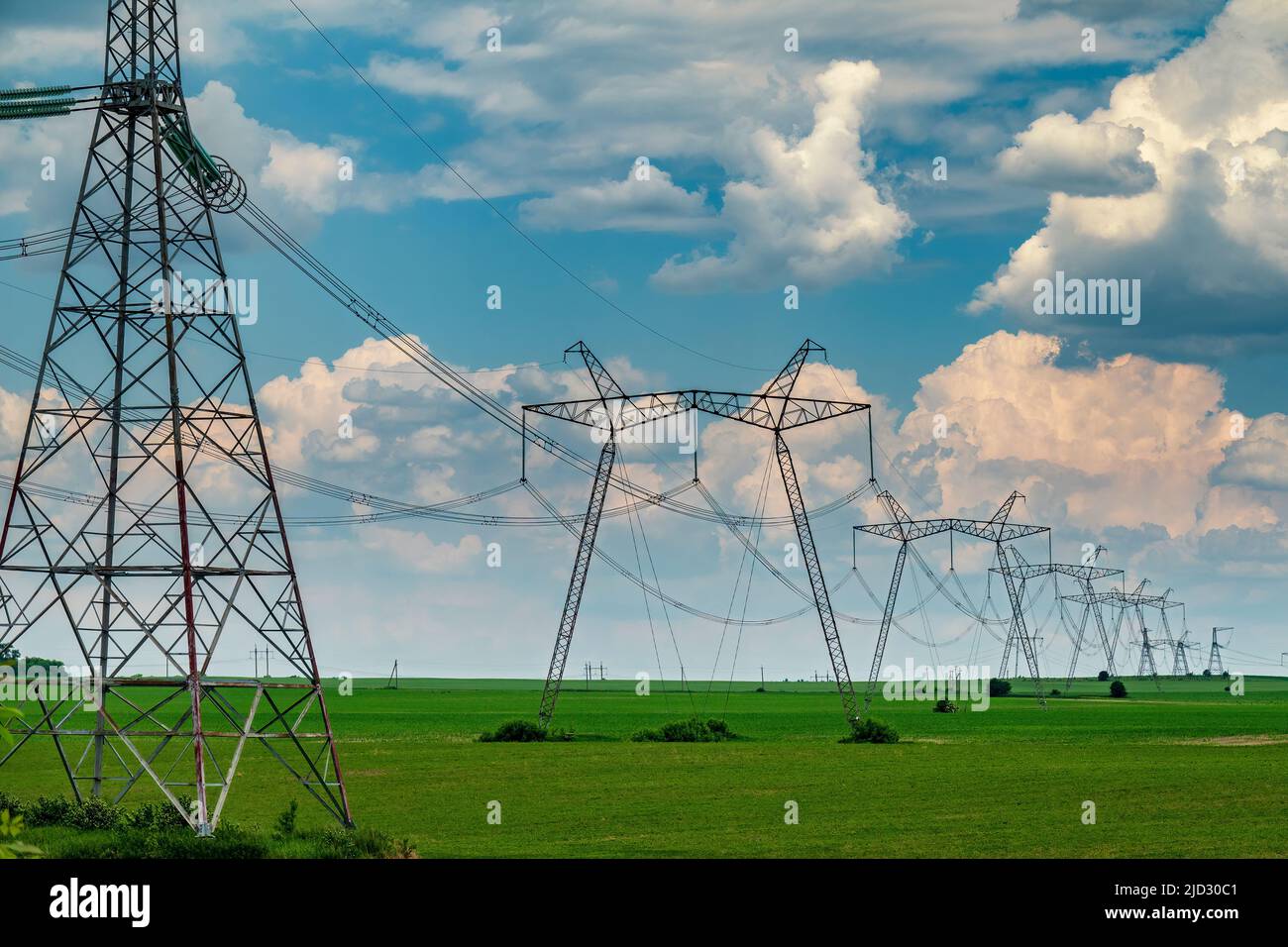 Row of power line support pylons on the green cultivated field with ...