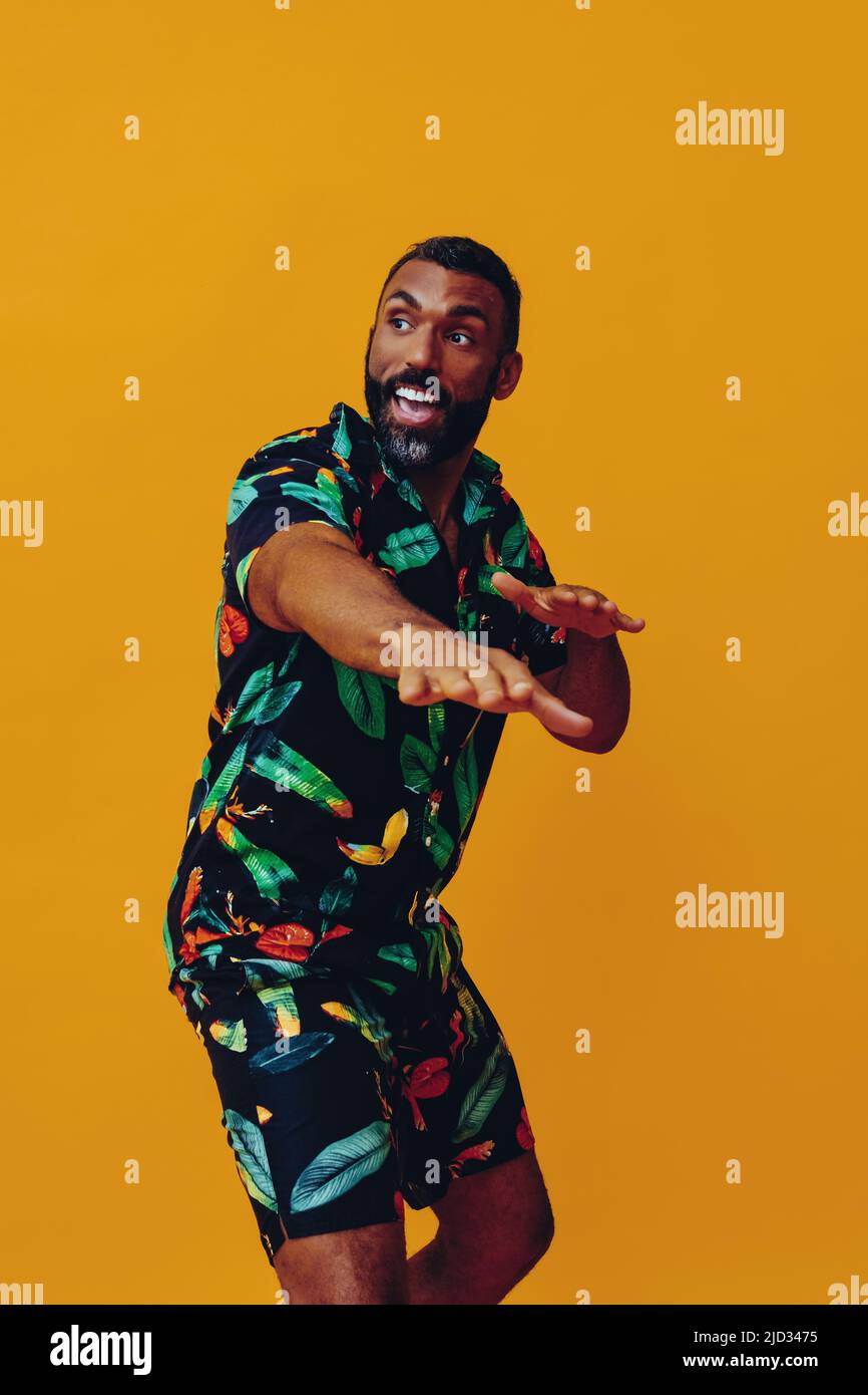 handsome bearded mid adult african american man smiling and dancing wearing Hawaiian shorts and shirt on vacation studio shot Stock Photo