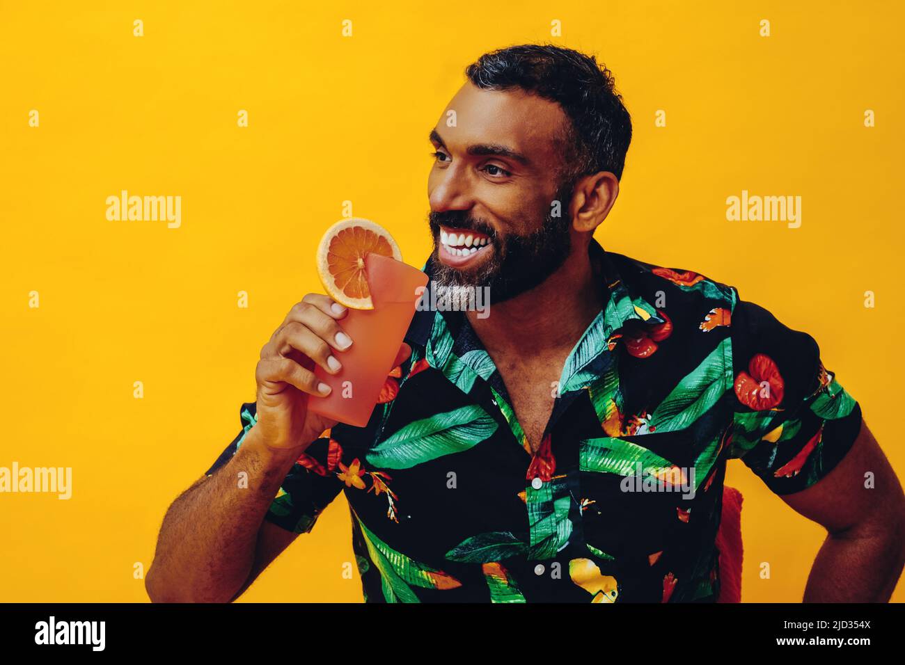 handsome bearded mid adult african american man smiling on vacation sitting on a chair drinking orange juice cocktail studio shot Stock Photo