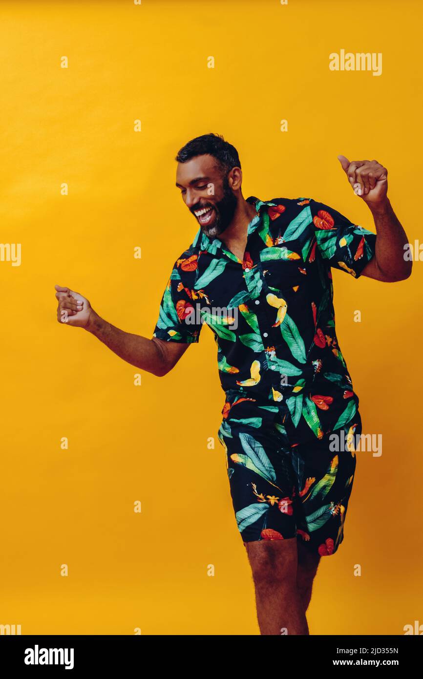 handsome bearded mid adult african american man smiling and dancing wearing Hawaiian shorts and shirt on vacation studio shot Stock Photo