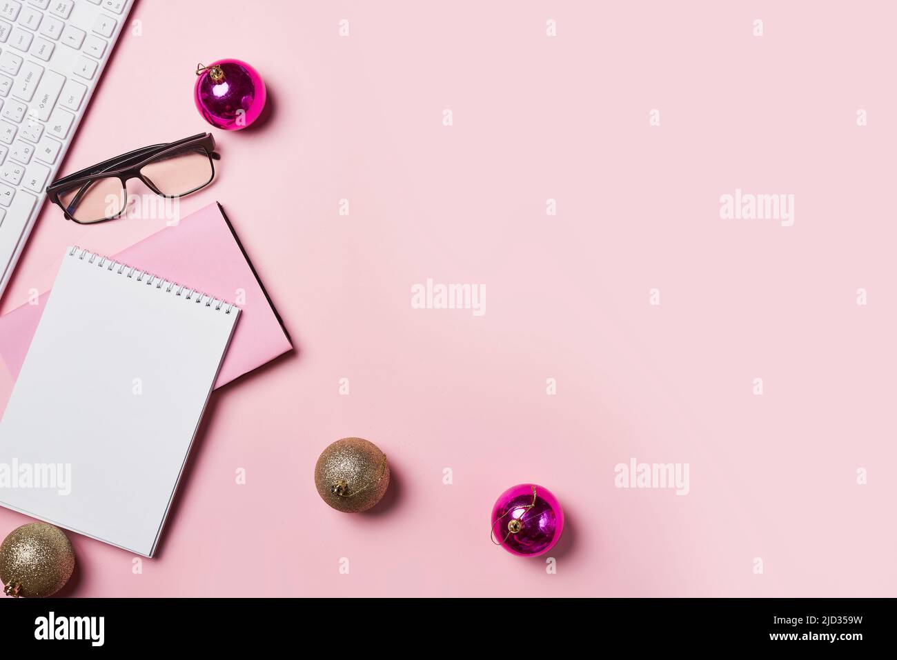 Home office table with Christmas decorations, coffee cup and notebook on pink backgraund. Flat lay, top view. Christmas workspace. Minimalism Stock Photo