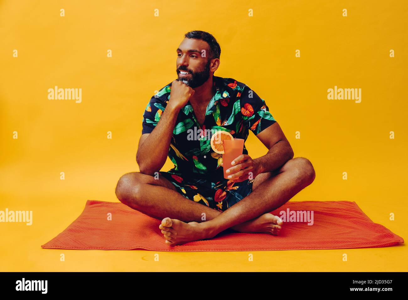 handsome bearded mid adult african american man smiling on vacation sitting on an orange towel, holding orange juice studio shot Stock Photo