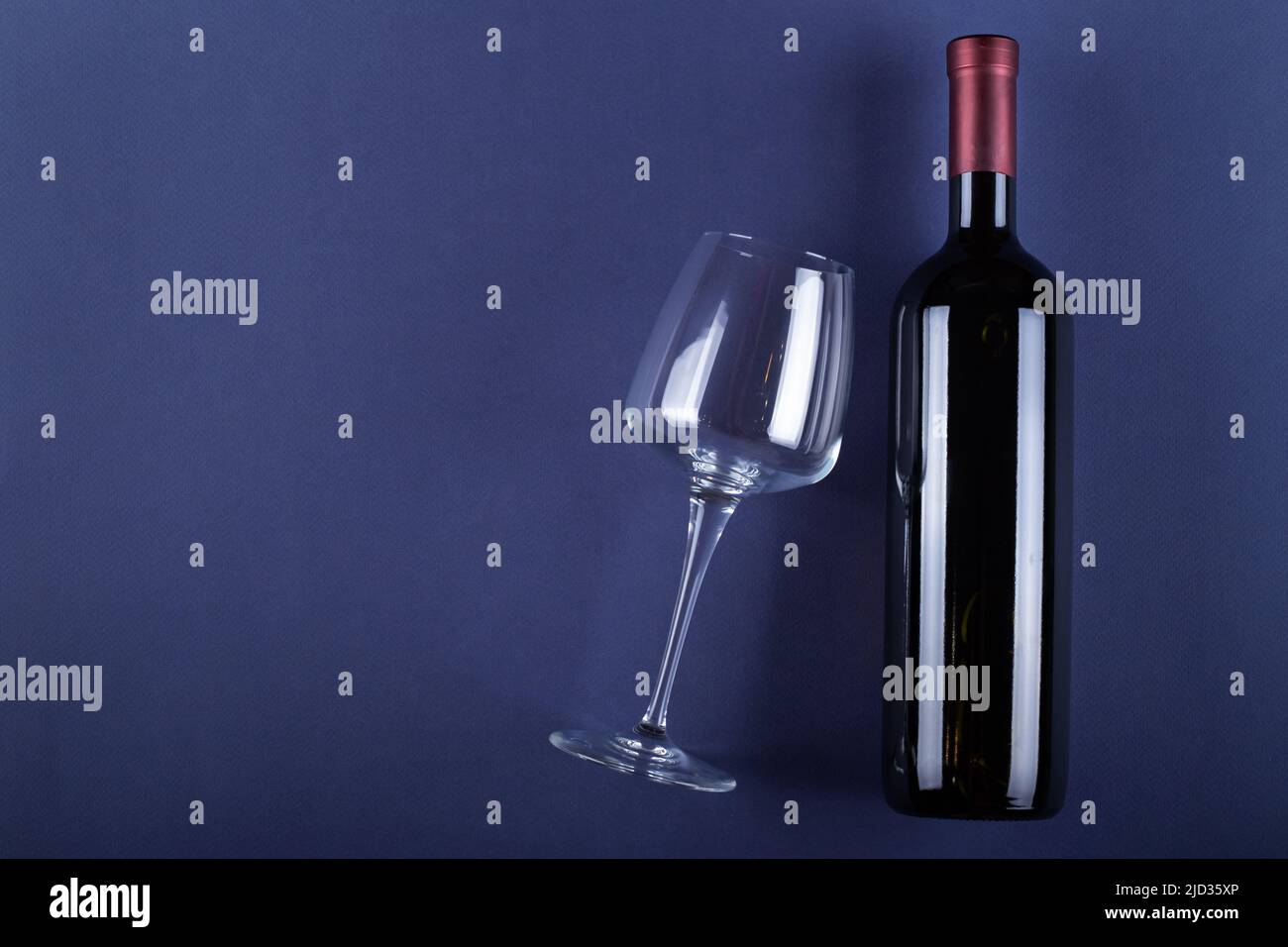 Bottle of red wine without a label and a glass empty on a purple paper ...