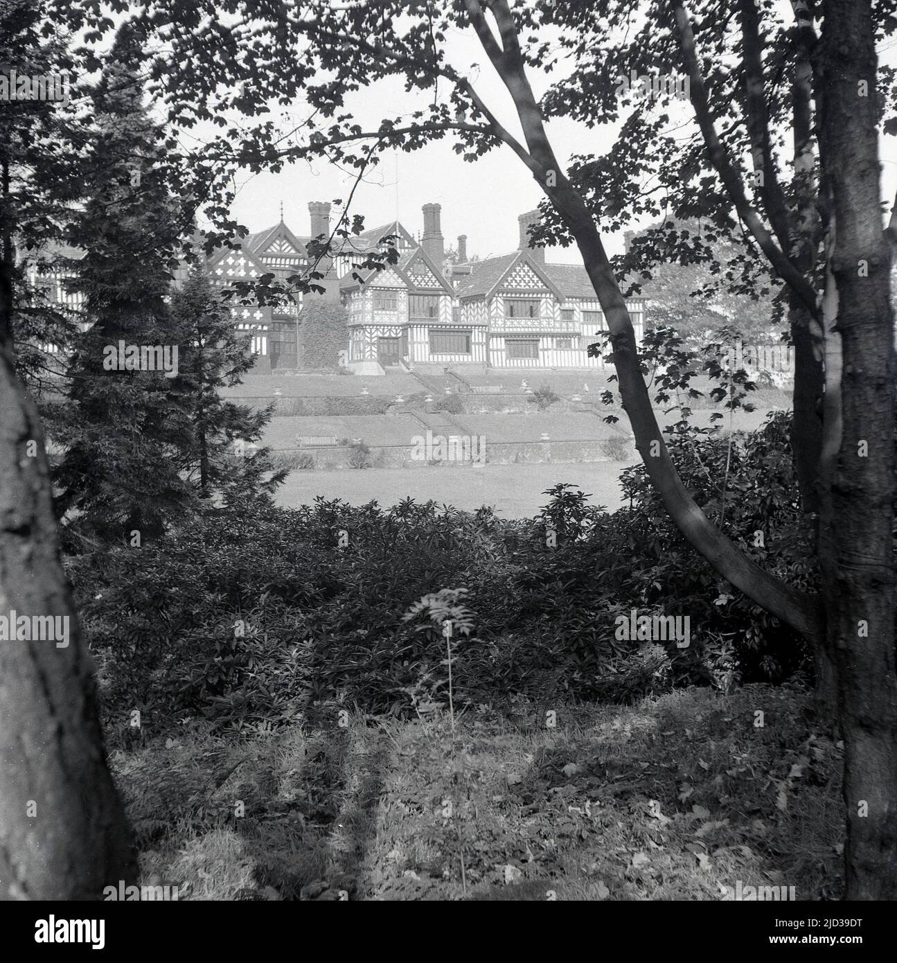 1940s, historical, distant  view through trees of Bramall Hall, Bramhall, Stockport, England, UK. A timber-framed Tudor manor house that dates back to the 14th century, with later additions, the house and surrounding parkland was acquired by the local authority in 1935 and became a museum. The Davenport family, which it is believed built the house, held the manor for over 500 years. Stock Photo