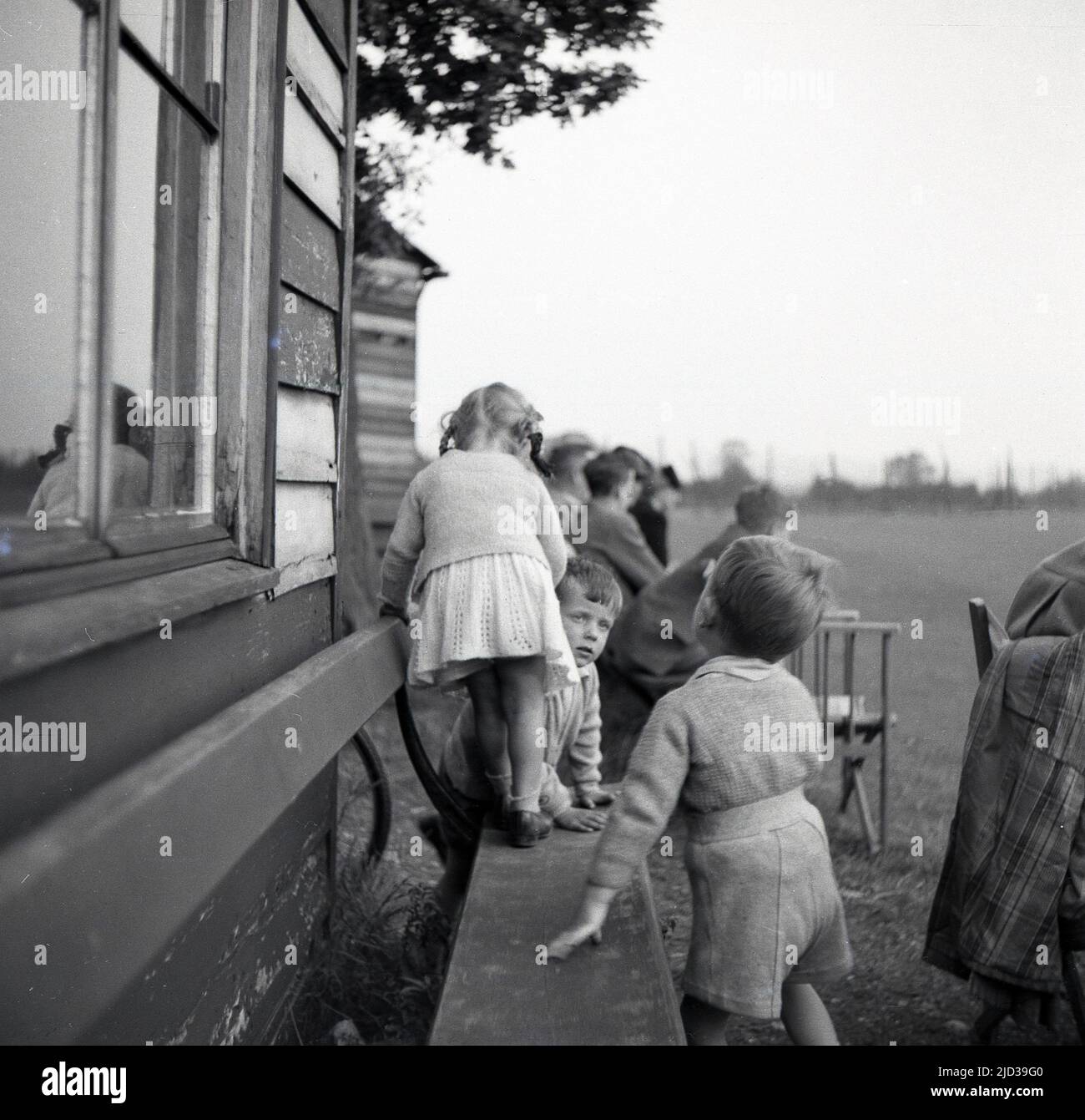 1950s, historical, children playing on a bench outside a wooden pavilion, at Bramhall Cricket Club, Bramhall, Stockport, England, UK. Stock Photo