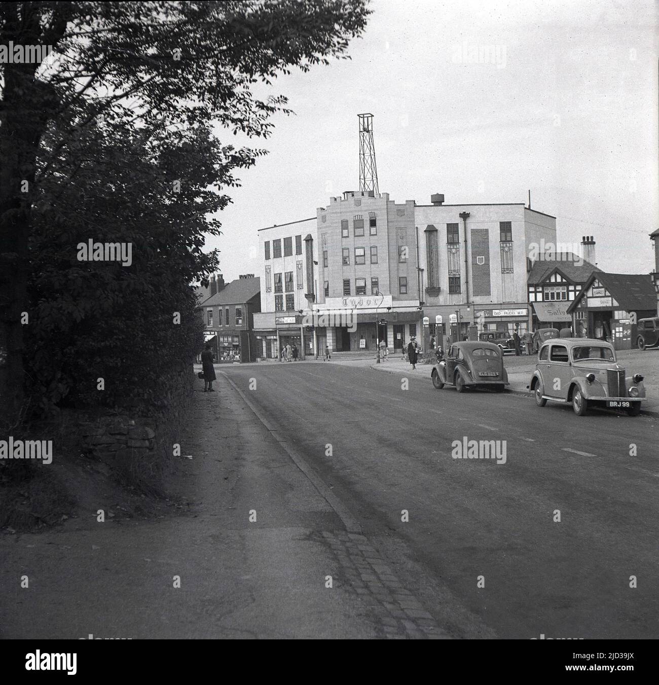 1940, historical, distance view of the Tudor cinema at Bramhall, Stockport, England, UK. Located on a corner site with Woodford Road and Meadway, the building was designed by architect George Clayton, with the auditorium decorated in a Tudor style and opened on 31st March 1935 with Clark Gable in “It Happened One Night”. This picture, taken in 1940, saw the film 'Dad Rudd MP' being shown. Cars of the era can be seen parked on the road. Stock Photo