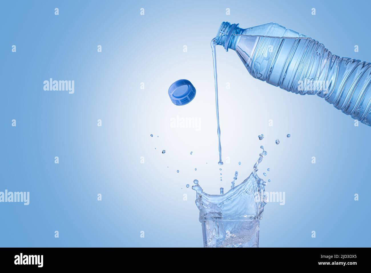 Bottle of mineral water pouring  into the glass isolated on blue background with copy space. The pure water for better health concept. Stock Photo
