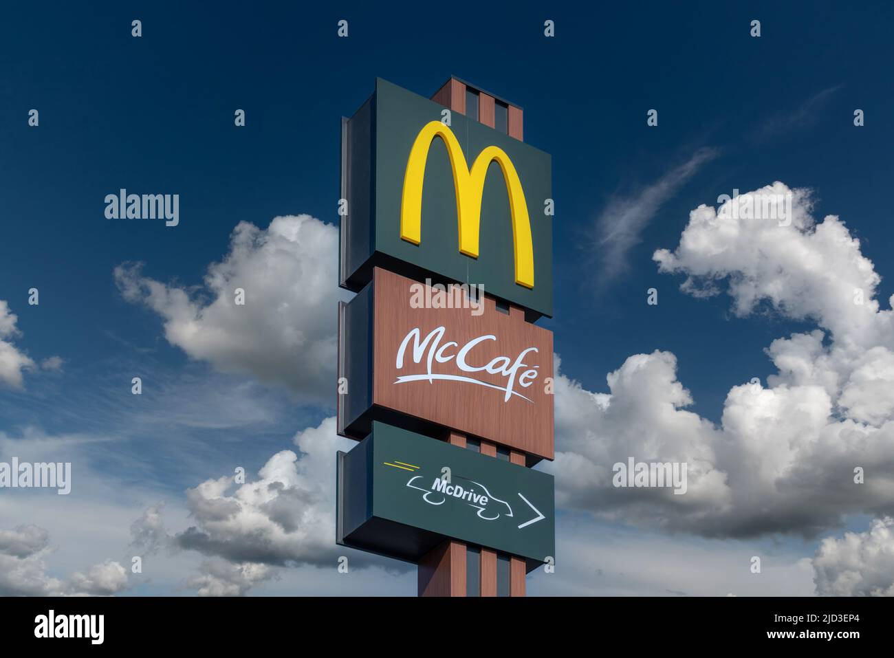 Savigliano, Italy - June 16, 2022: McDonald's sign with McCafe and McDrive logo on blue sky with white clouds. The McDonald's Corporation is world's l Stock Photo