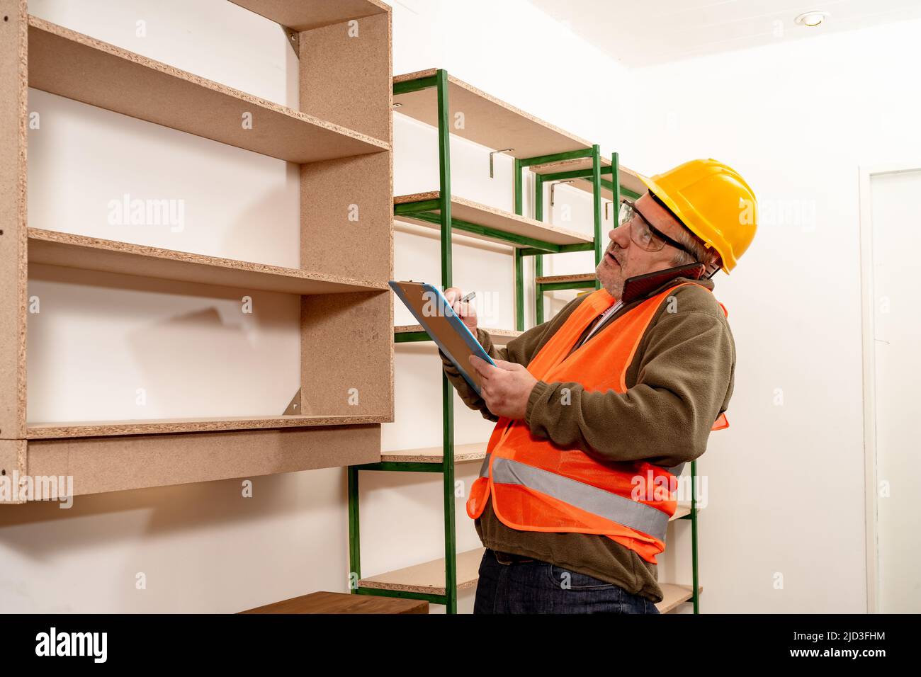 Mature Caucasian inspector talking on cell phone while checking the status and progress of the work in the work office. Concept of labor organization, Stock Photo