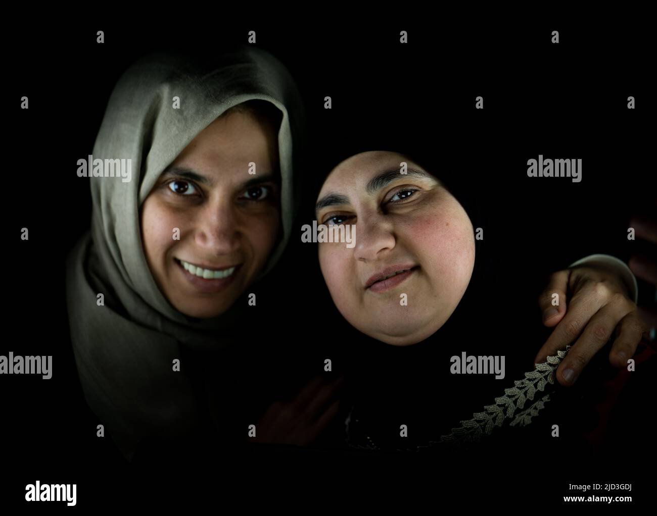 Two happy Muslim woman in hug together on black background. High ...