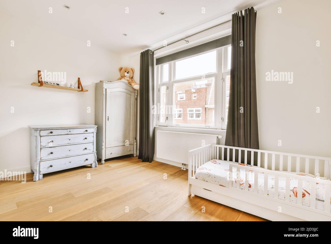 Interior of white room with baby crib near window with blue chest of