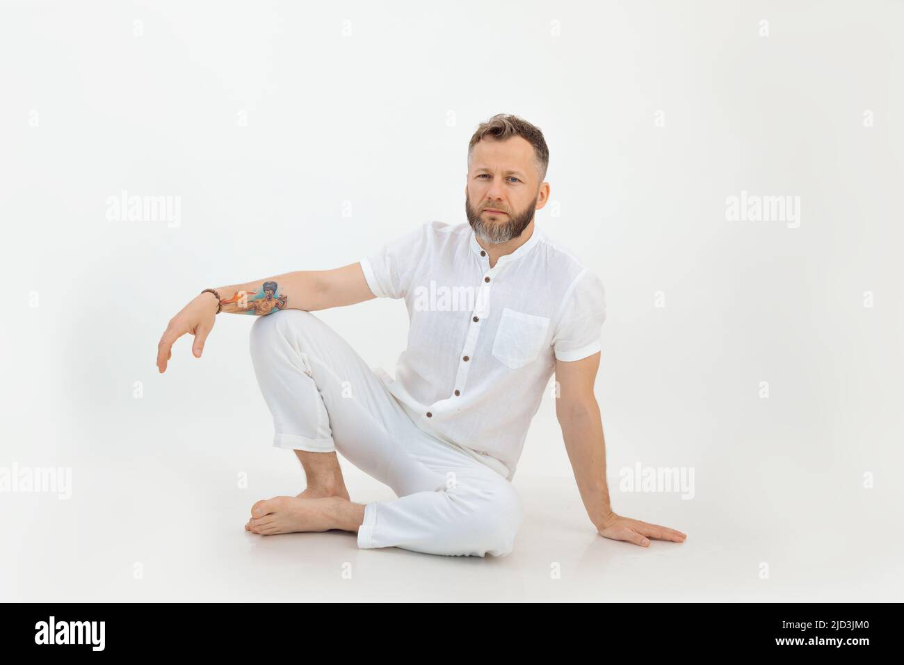 Bearded barefoot thoughtful man with tattoo sitting on the floor. Small business, yoga and pilates sports studio coach Stock Photo