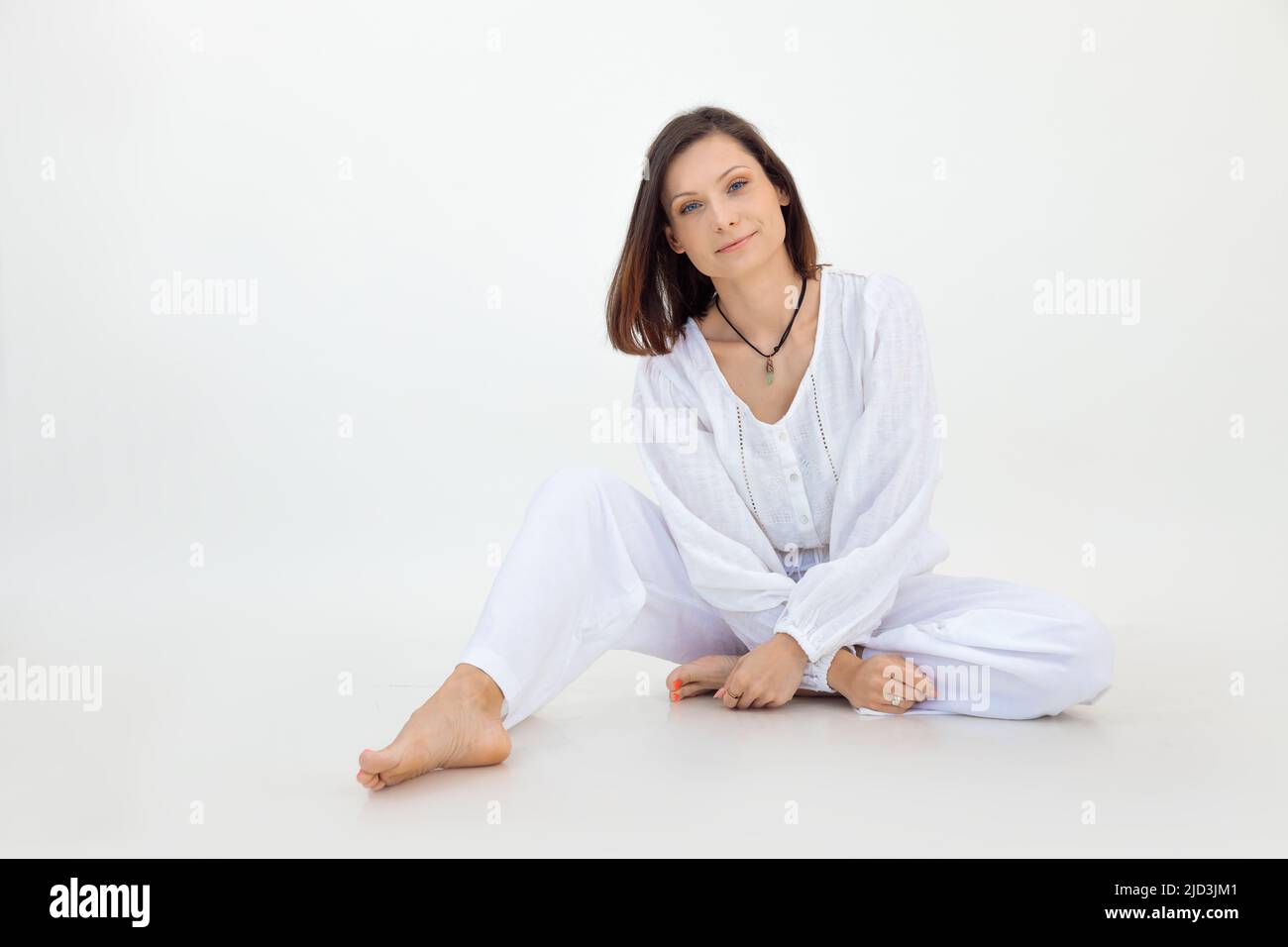 Attractive barefoot brown-haired woman wearing white outfit in white studio. Body and skin care cosmetics ad. Copy space Stock Photo