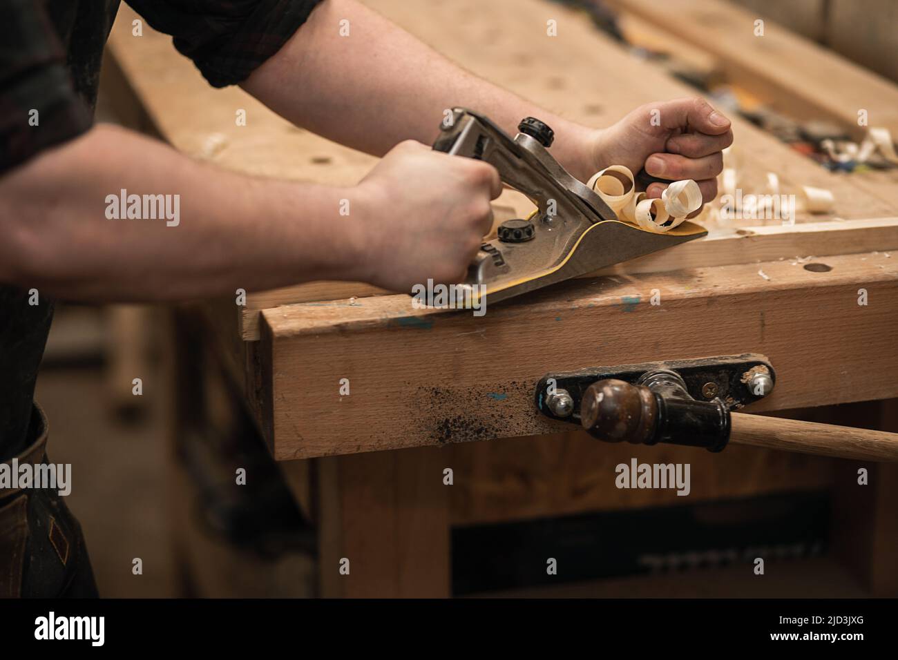 Close-up joiner hands working with wood timber, cutting, sharping by plane, shavings flying around workbench. Business Stock Photo