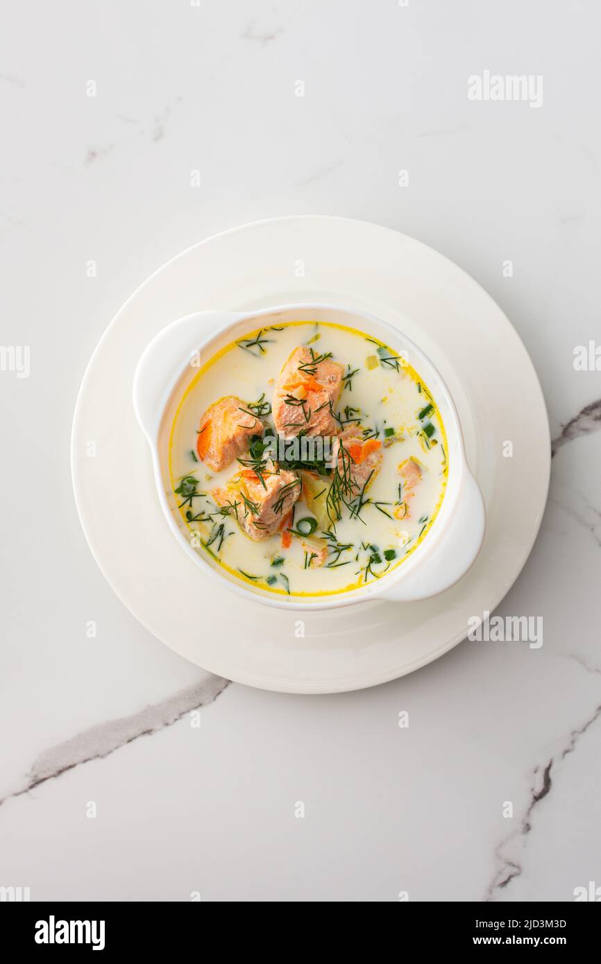 Norwegian red salmon fish soup with vegetables, herbs and cream, top view of a bowl of soup on a white marble background Stock Photo