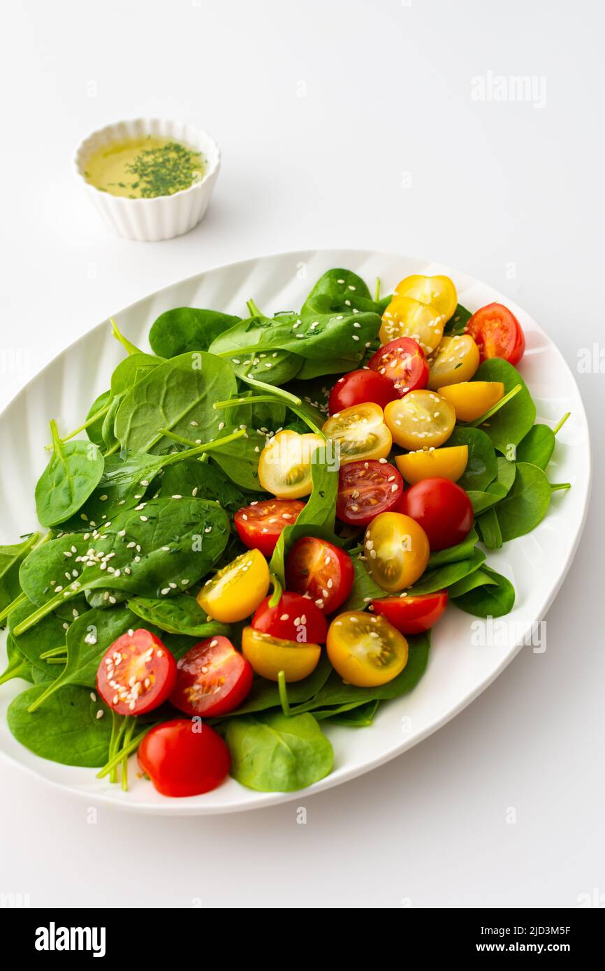 Salad with yellow and red tomatoes and spinach, top view of an oval plate with lettuce on a white background Stock Photo