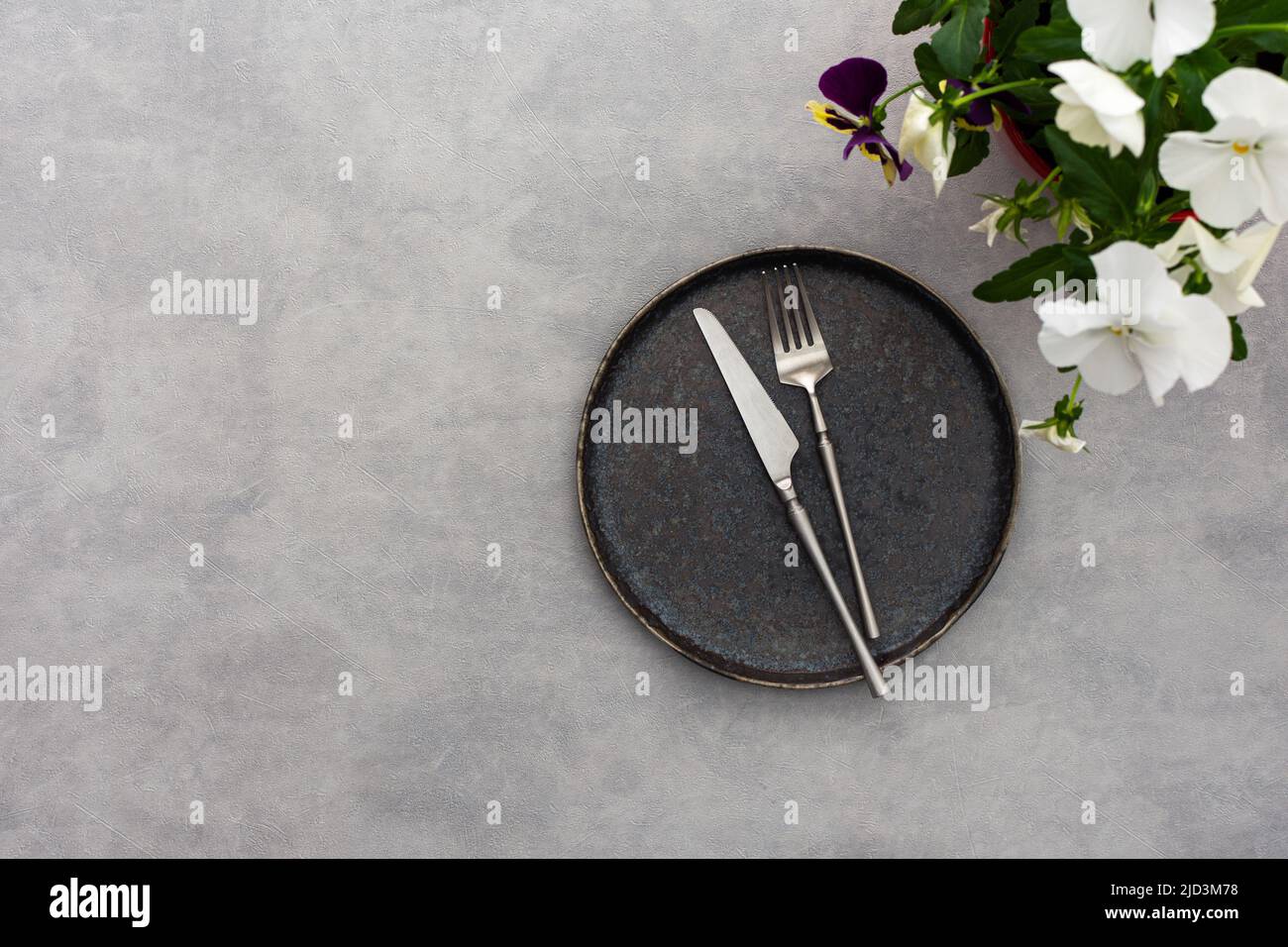 Table setting, empty plate and cutlery on the gray background, top view of the served table decorated with pansies flowers Stock Photo