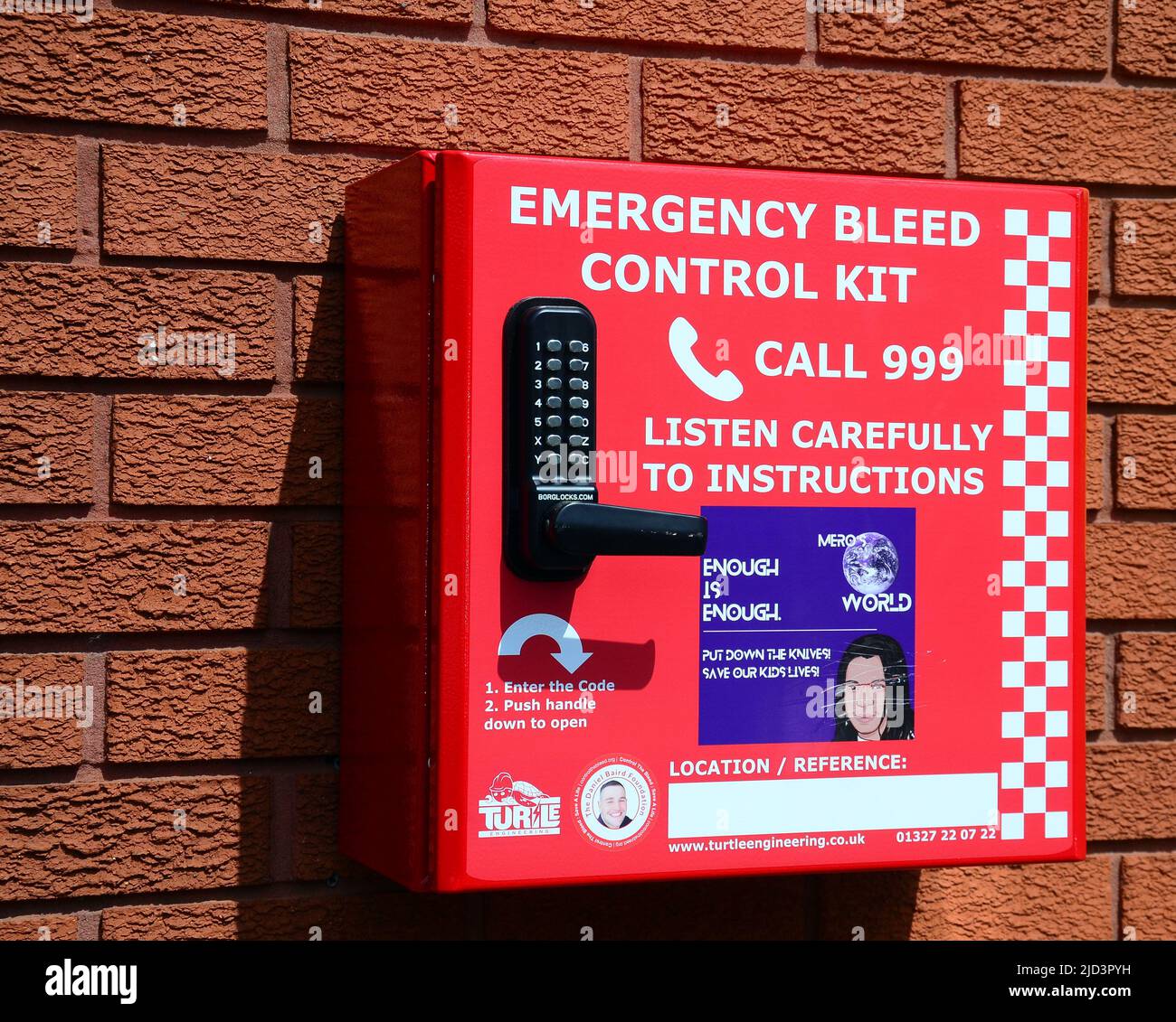 Emergency bleed control kit mounted in a red box on a brick wall with instructions on the front to call 999 emergency line in Manchester, England, UK. Stock Photo