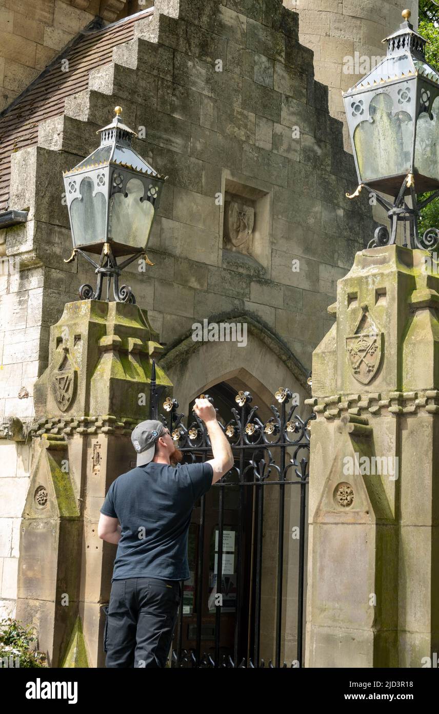 Young man in reversed baseball cap hand panting the gold tops to railing at the entrance to Museum Gardens in York, North Yorkshire, England Stock Photo
