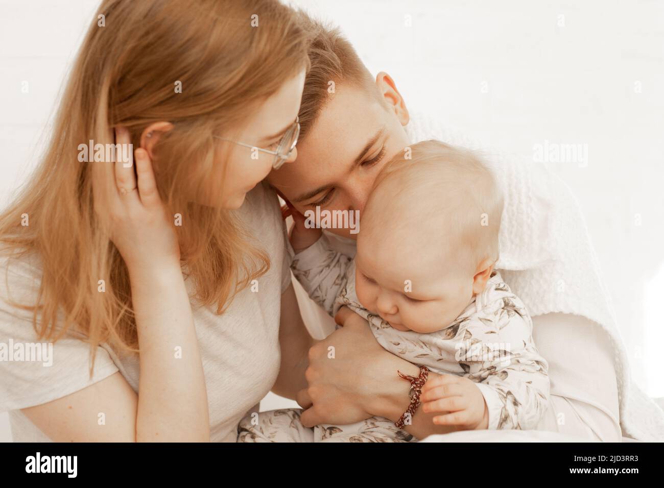Young mother and father embrace little baby, have fun and enjoy on white background. Cute relationship between parents and infant child closeup, free Stock Photo