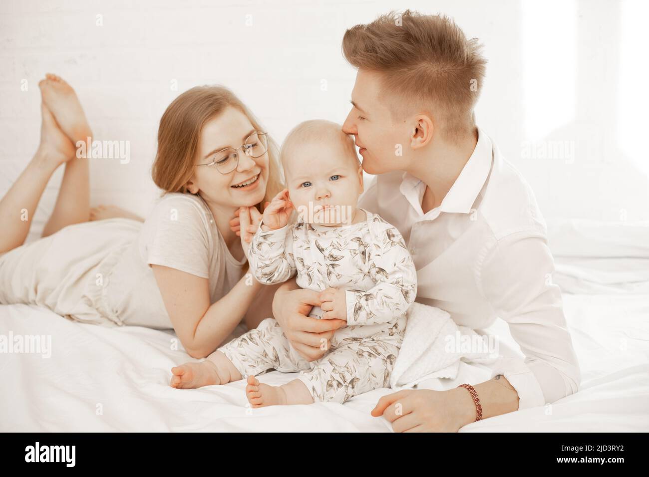 Young mother and father lay with little baby on bed, embrace and enjoy on white background. Cute relationship between parents and infant child, free Stock Photo