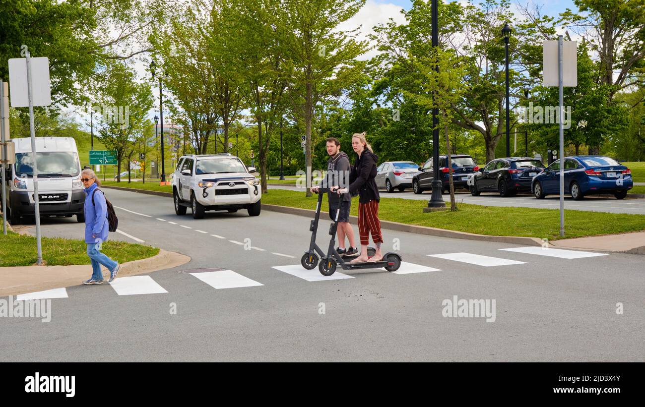 Two people on electric scooters using a pedestrian crossing to go through intersection Stock Photo