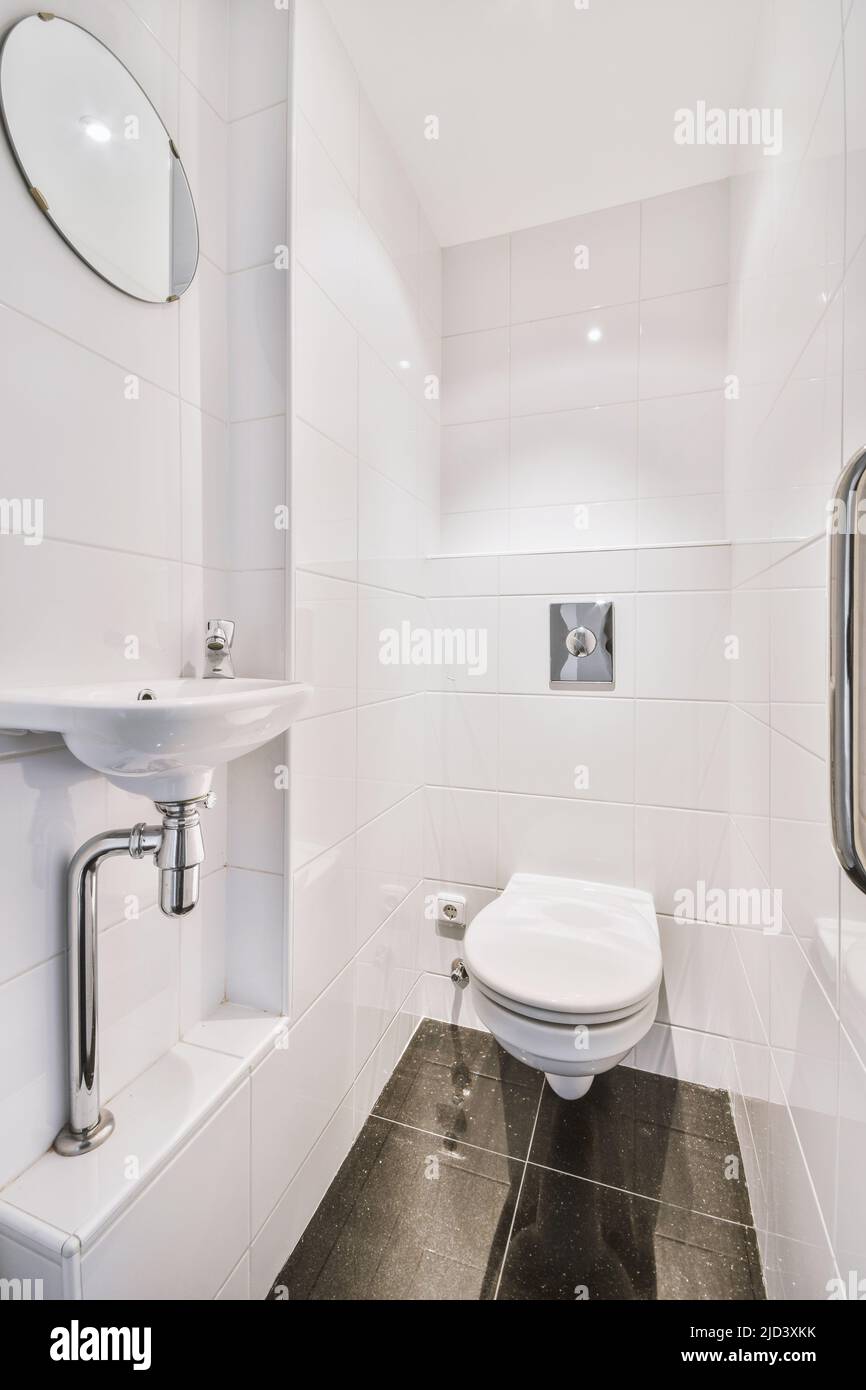 Interior of narrow restroom with sink and wall hung toilet with white