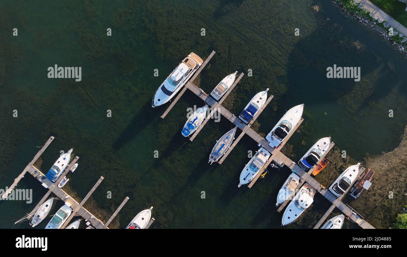 A direct overhead aerial photo above a sunny dock filled with moored leisure craft and yachts are seen below at dusk. Stock Photo