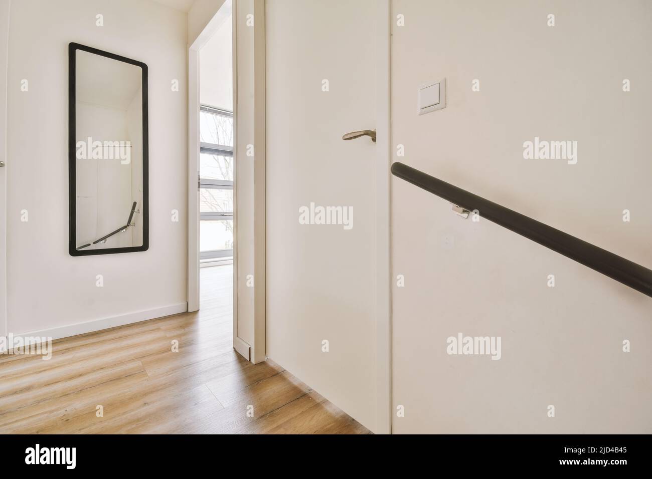 Narrow hallway with black framed mirror, white walls and doors leading