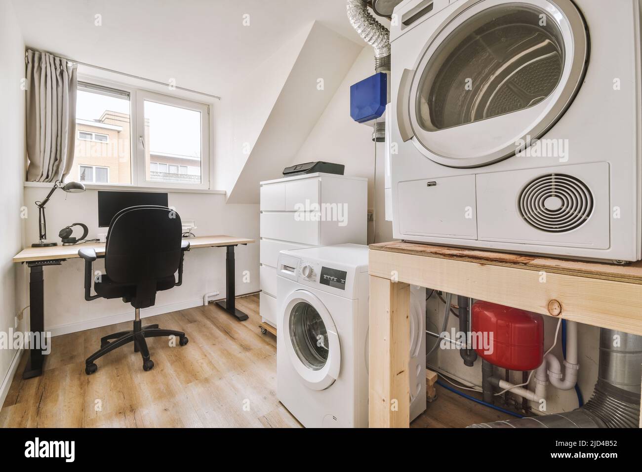 A comfortable armchair next to a table with computer monitors located along the window next to a closet in a room with washing machines Stock Photo