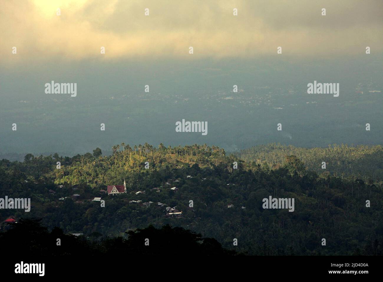 A distant view of the landscape of a village surrounded by forest and agricultural plantations in Minahasa, North Sulawesi, Indonesia. Stock Photo