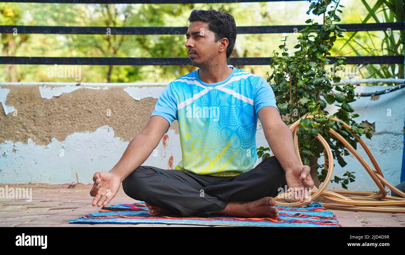 Full of joy young Indian man wearing sports clothes blue shirt and black tights in lotus position Stock Photo