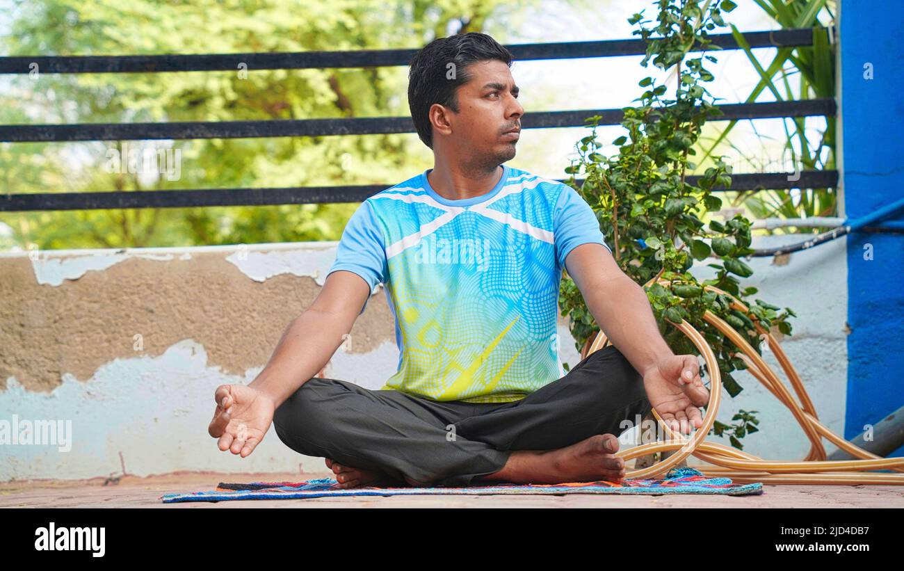 young Indian man sitting in lotus position on her yoga mat in meditation during sunrise Stock Photo